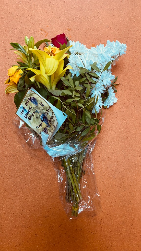The bouquet of flowers after 10 days. It shows signs of age and wear but is not in bad condition. It lies on the floor of Loula's studio, which is bright orange.