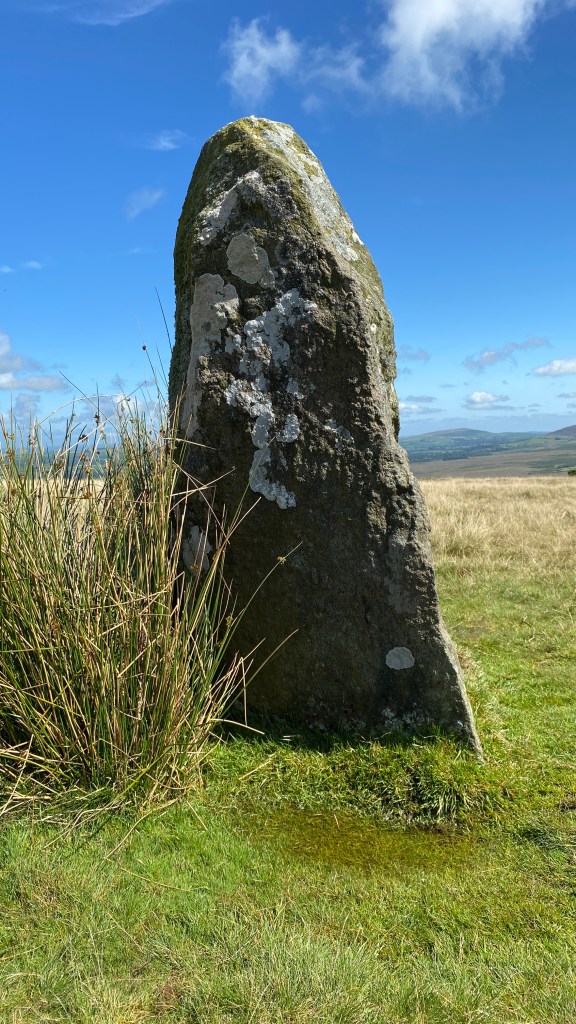 a standing stone against a a hilly landscape in the sunshine