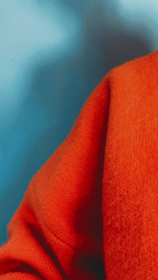 the sleeve of a bright orange woollen jumper against a blue wall